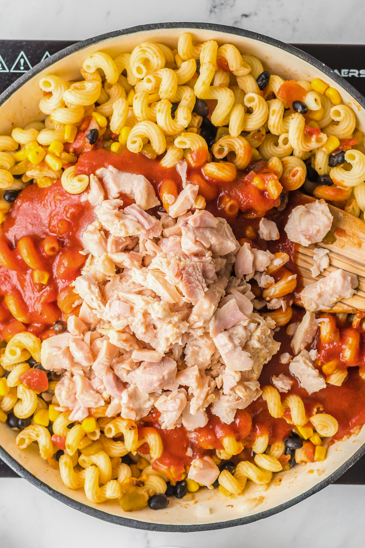 Cooked pasta, enchilada sauce, chicken, and other ingredients in a large skillet.