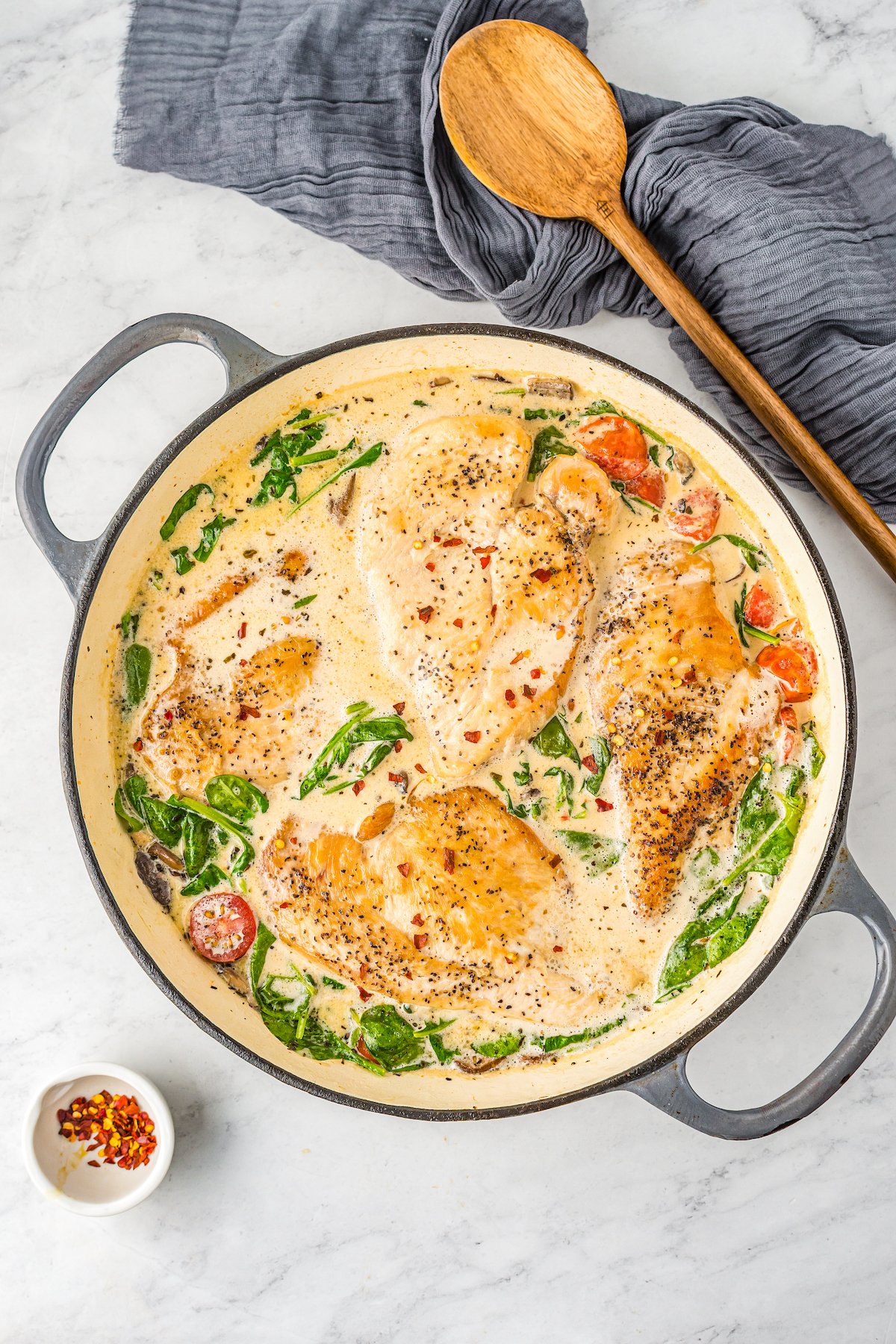An overhead shot of a two-handled skillet of cooked chicken in Florentine sauce.