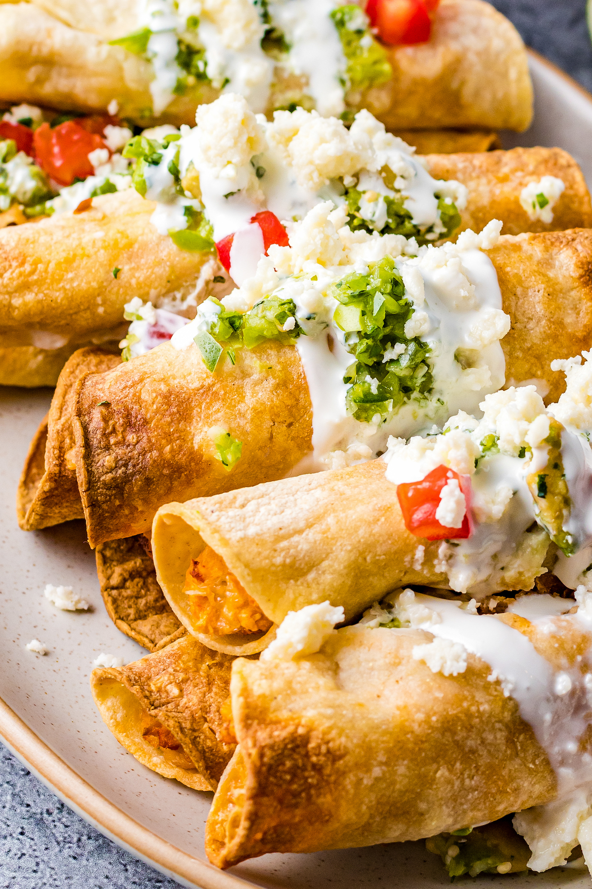 A platter of chicken taquitos garnished with crema and other toppings.