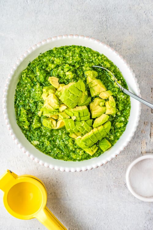 Diced avocado being stirred into a bowl of salsa verde.