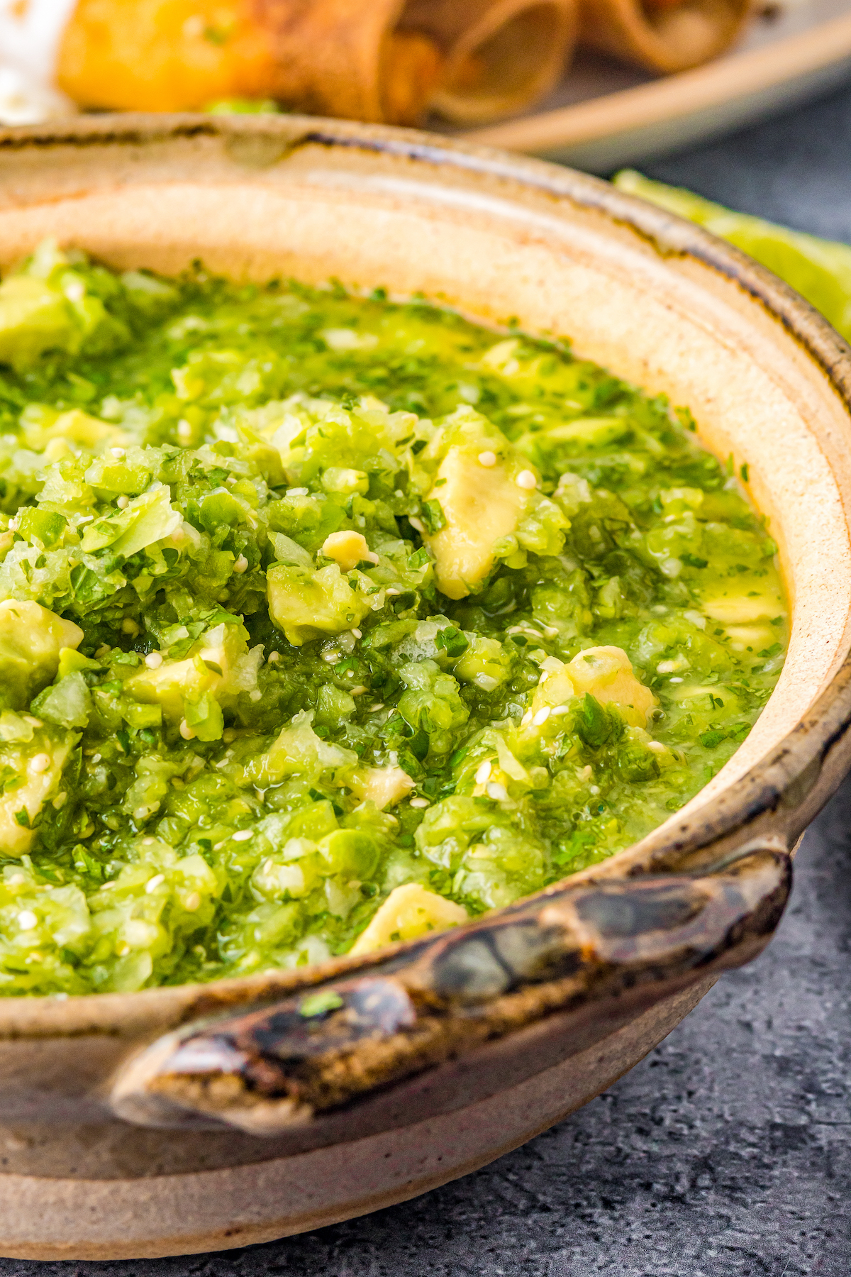 Close-up shot of chunky green salsa in an earthenware bowl.