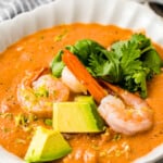 Close-up shot of shrimp bisque garnished with herbs, avocado, shrimp, and more.