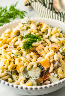 Close-up shot of pasta salad garnished with fresh dill in an off-white serving dish.