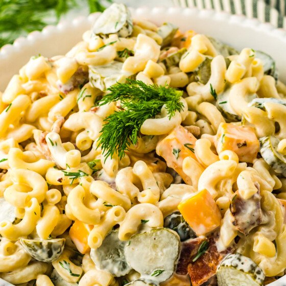 Close-up shot of pasta salad garnished with fresh dill in an off-white serving dish.