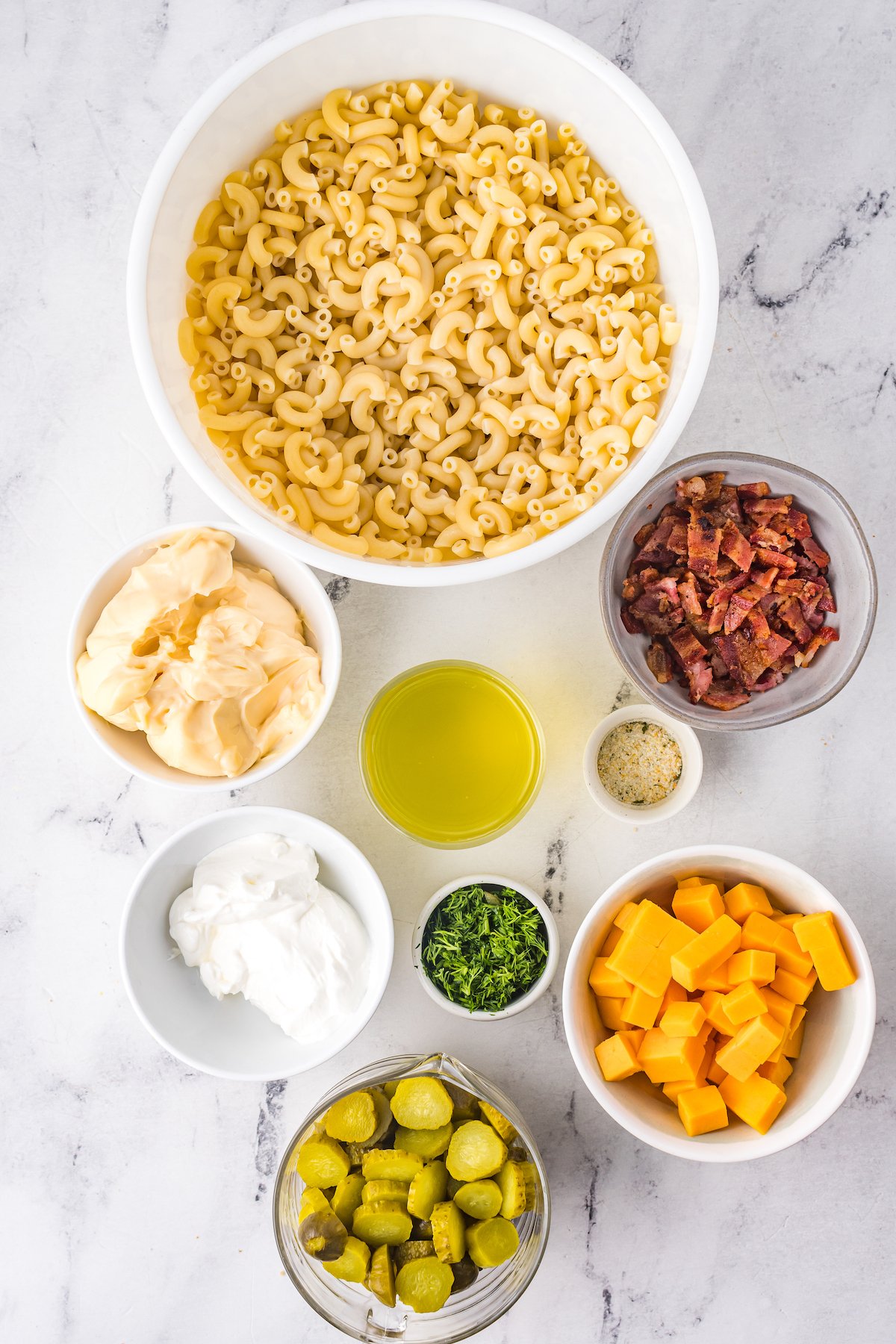 From top: Cooked elbow pasta, bacon bits, garlic powder, cheddar cheese, minced fresh dill, sliced dill pickles, sour cream, pickle juice, mayonnaise.