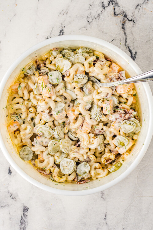 A cold pasta salad with pickles, cheese, and creamy dressing.