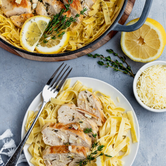 A plate of lemon thyme chicken pasta, next to a skillet of chicken in lemon garlic sauce.