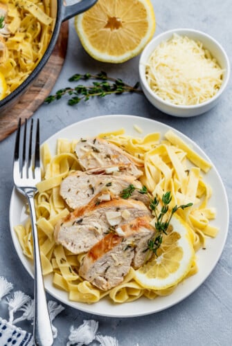 Lemon thyme chicken and pasta served on a plate next to a bowl of grated parmesan cheese.