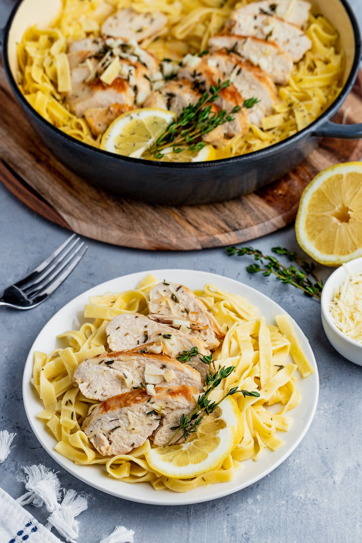 Lemon thyme chicken and pasta served on a plate next to a large bowl of chicken pasta.