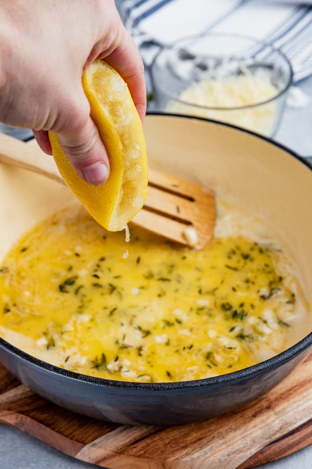A hand squeezes the juice from half a lemon into a pan with melted butter and thyme.