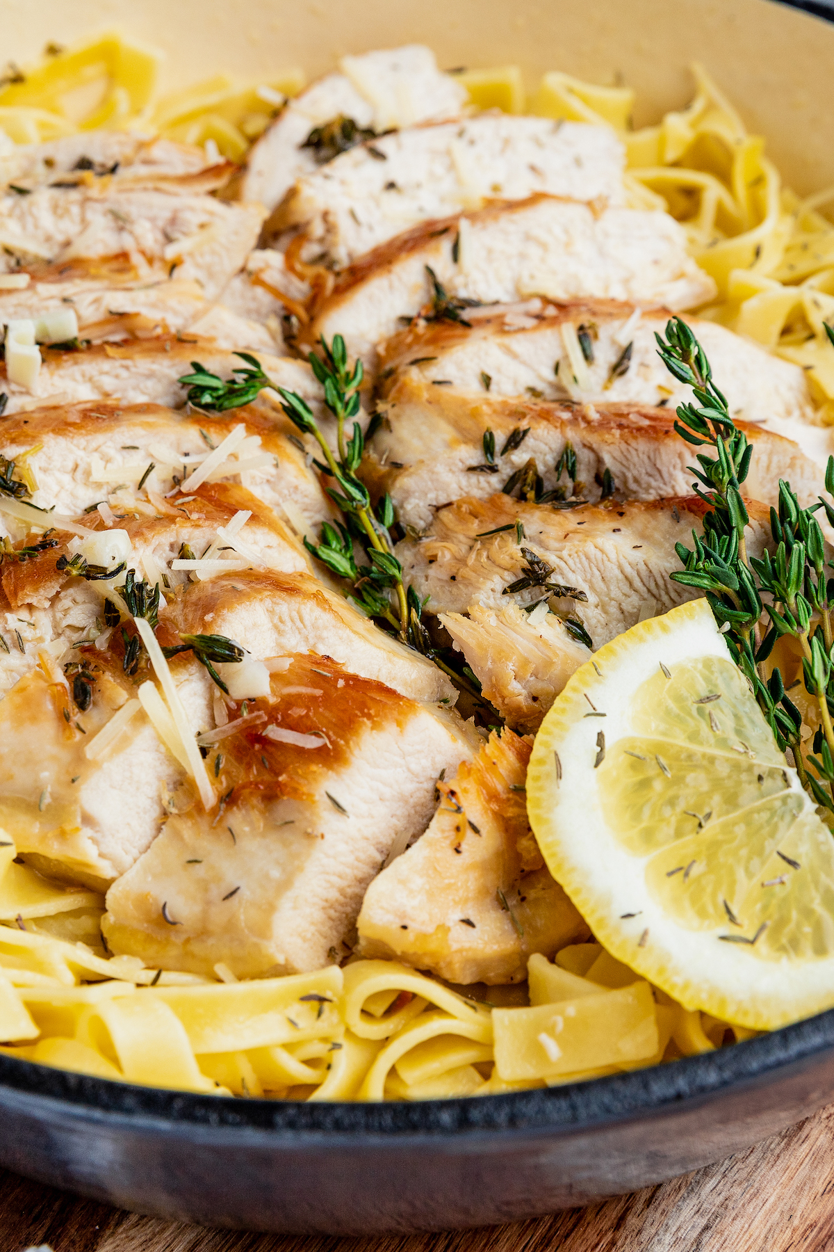 Sliced chicken served over a plate of pasta tossed in a lemon white wine sauce, garnished with a lemon slice.