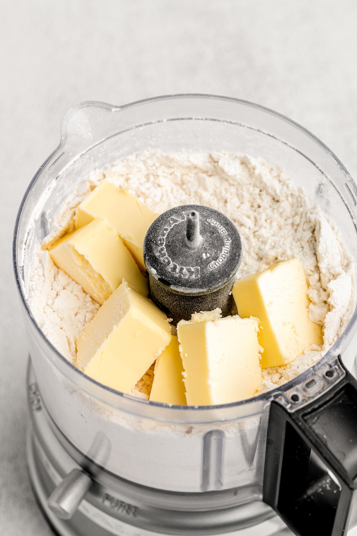 Butter sticks are added to the flour mixture in a food processor.