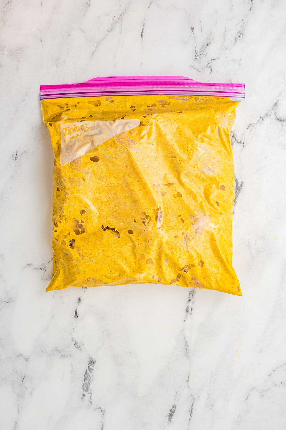 A ziploc bag full of yellow-gold creamy marinade and chicken.