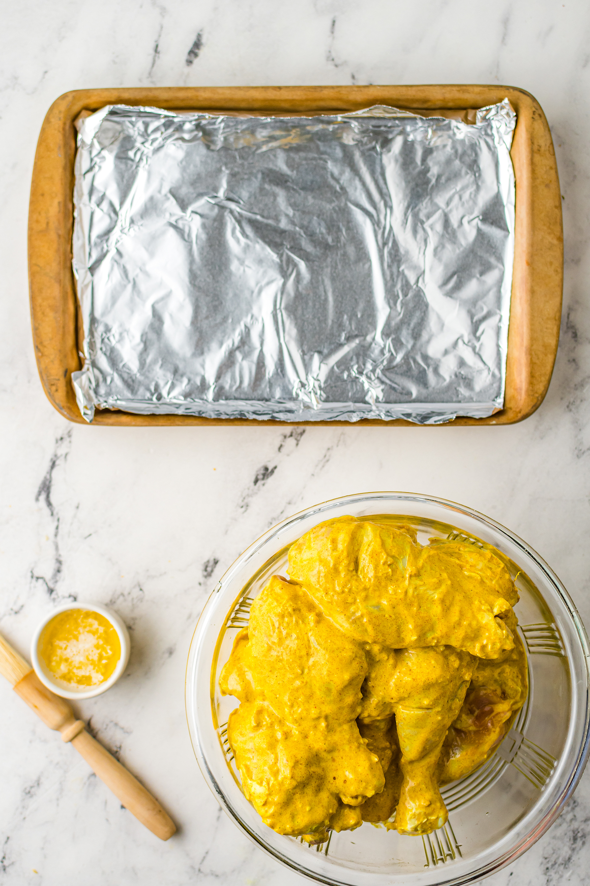 A bowl of marinated chicken next to a foil-lined baking sheet.