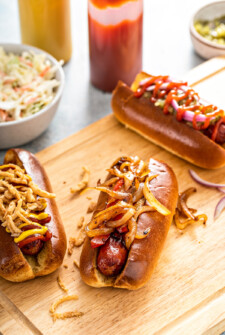 Air fryer hot dogs on a wooden cutting board garnished with various hot dog toppings.