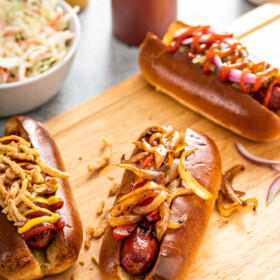 Air fryer hot dogs on a wooden cutting board garnished with various hot dog toppings.