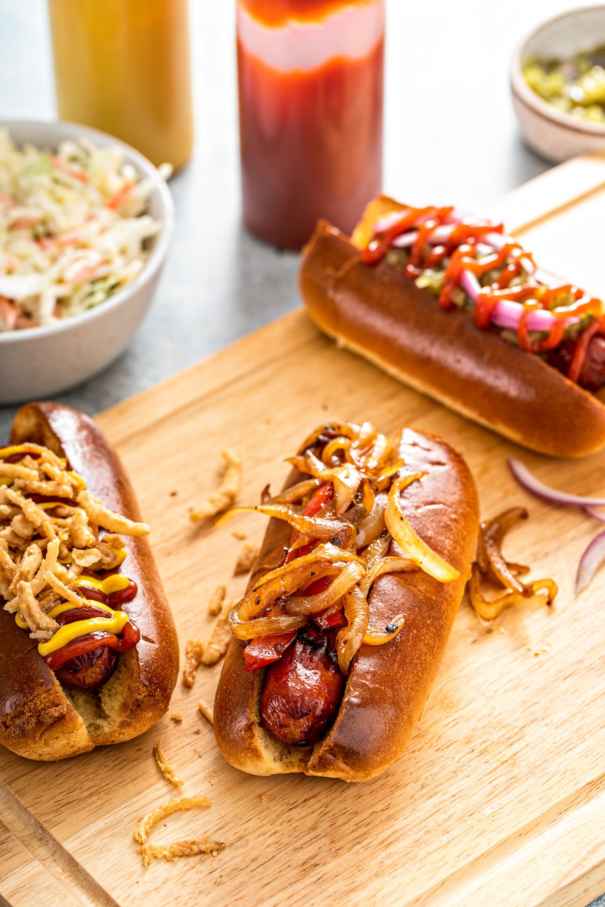 Air fryer hot dogs on a wooden cutting board garnished with various hot dog toppings.