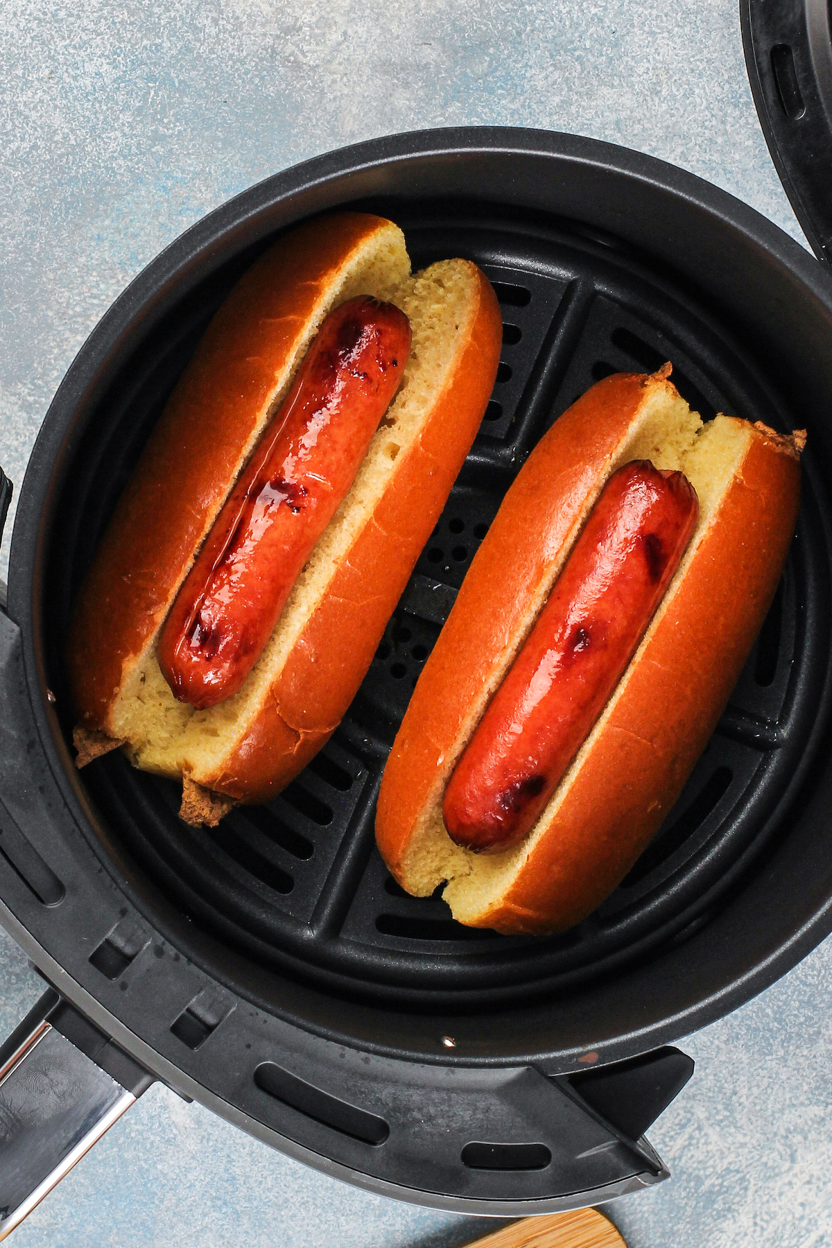 Hot dogs in buns inside an air fryer basket.