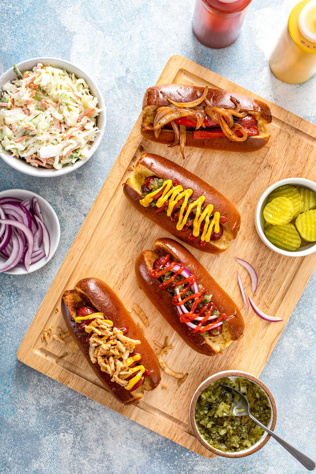 Top view of air fryer hot dogs on a wooden cutting board garnished with various hot dog toppings.