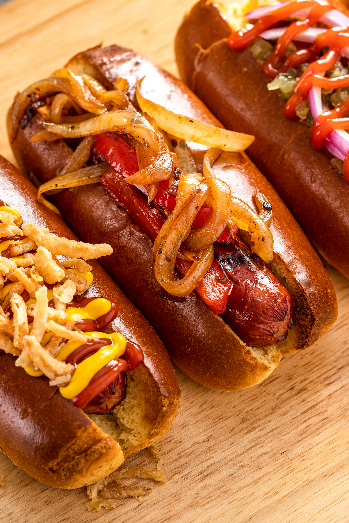 Close up of air fryer hot dogs in buns, garnished with onions and various hot dog toppings.