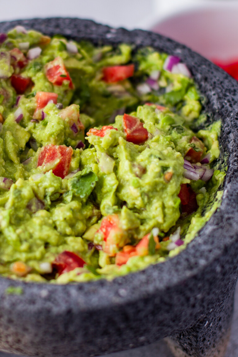 Close-up shot of avocado dip in a molcajete, with tomatoes.