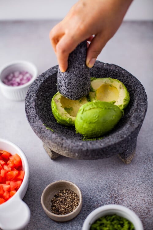 Avocado halves in a molcajete, being mashed.
