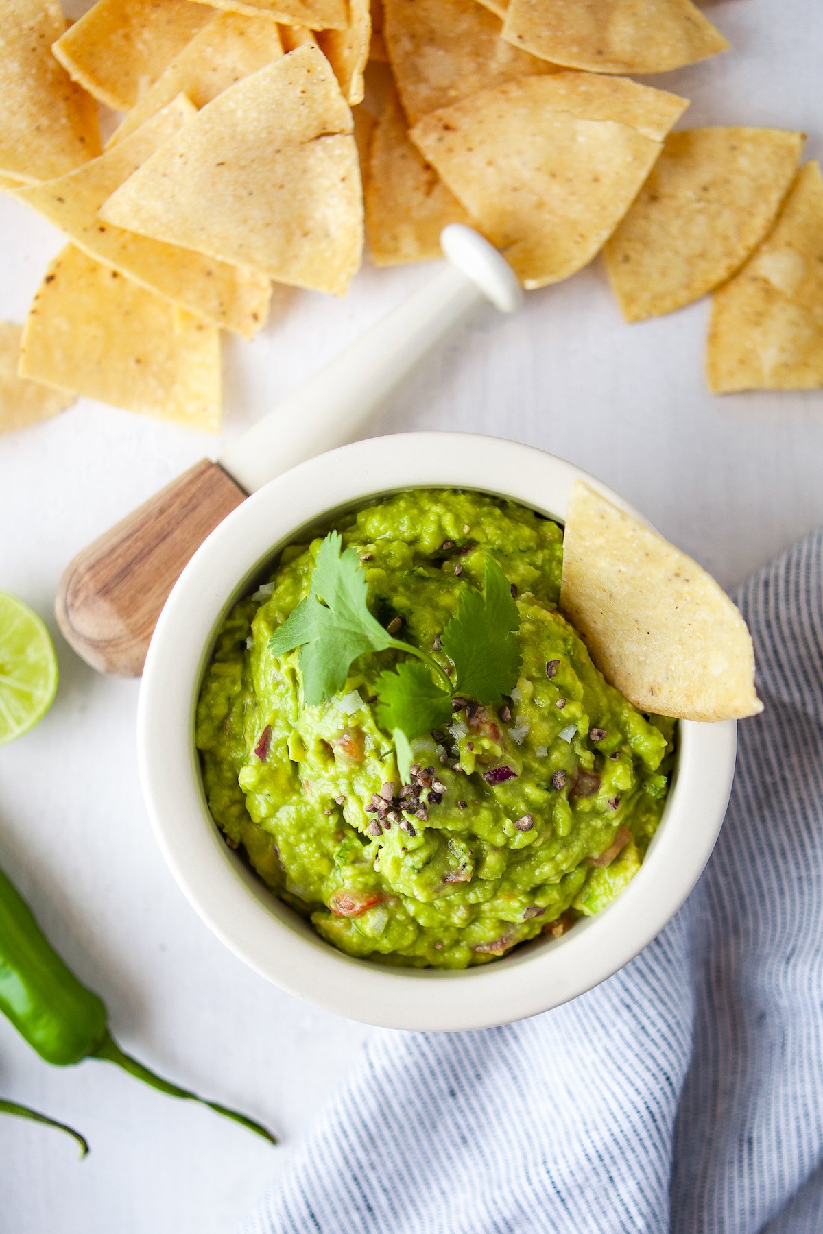 A bowl of guacamole with a tortilla chip garnish. More tortilla chips are scattered across the table.