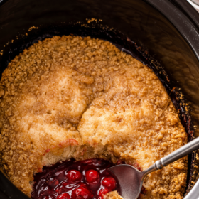 Cherry cobbler in a crockpot with a cutting board.