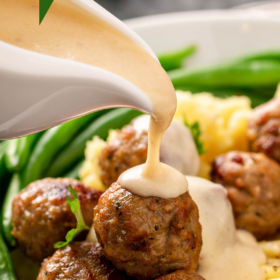Meatballs on a bed of mashed potatoes on a white plate cream sauce poured on top of the meatballs.