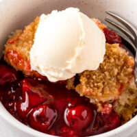 Crockpot cherry cobbler with vanilla ice cream in a white bowl.