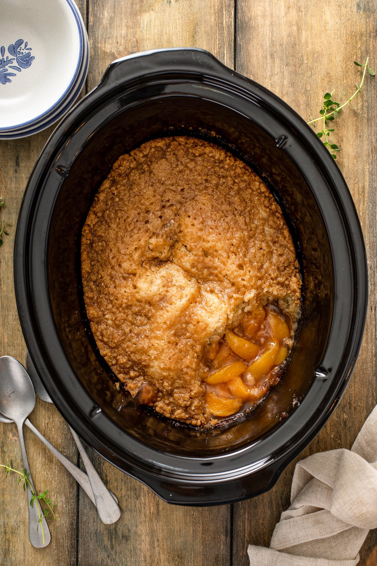Cooked peach cobbler inside a crock pot with a scoop missing from the corner.