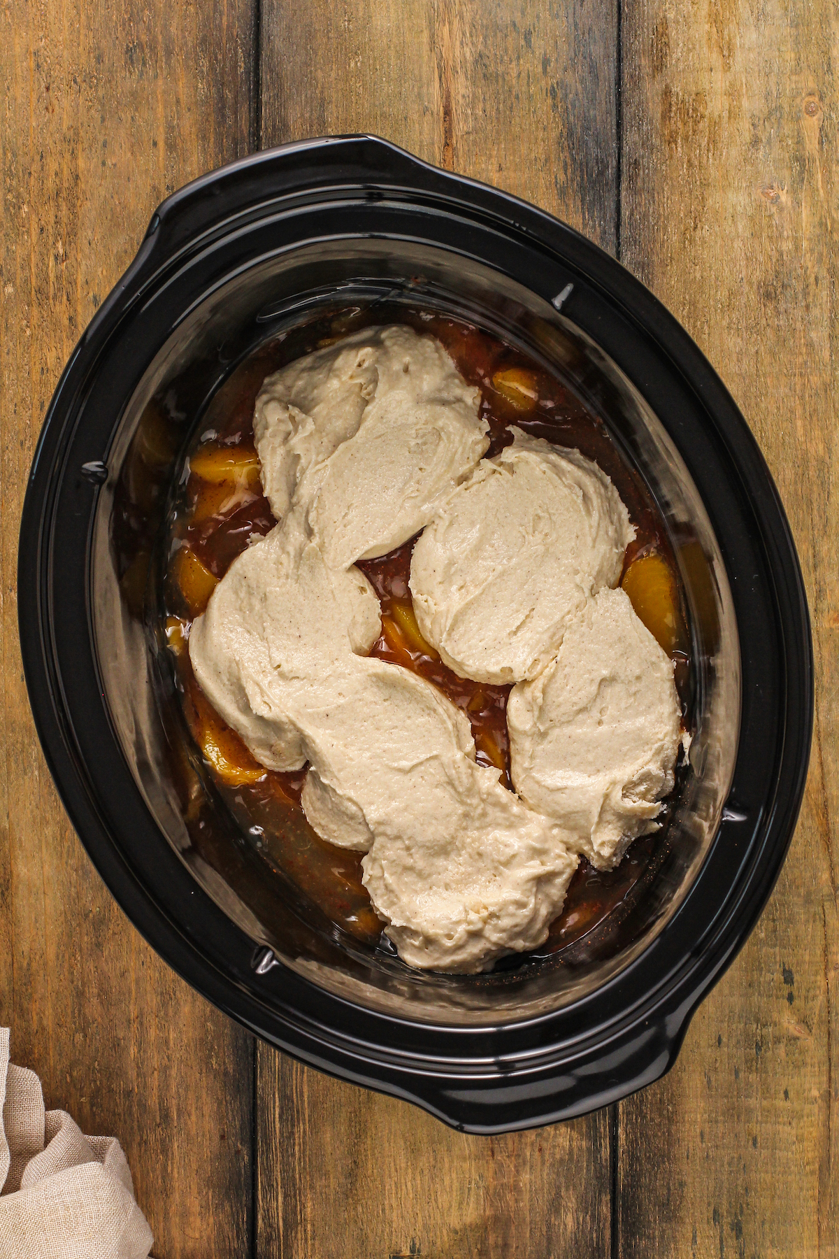Peach filling topped with spoonfuls of cobbler batter inside a crock pot.