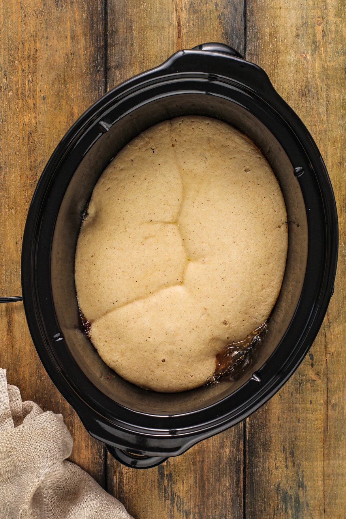 Partially cooked peach cobbler inside a crock pot.