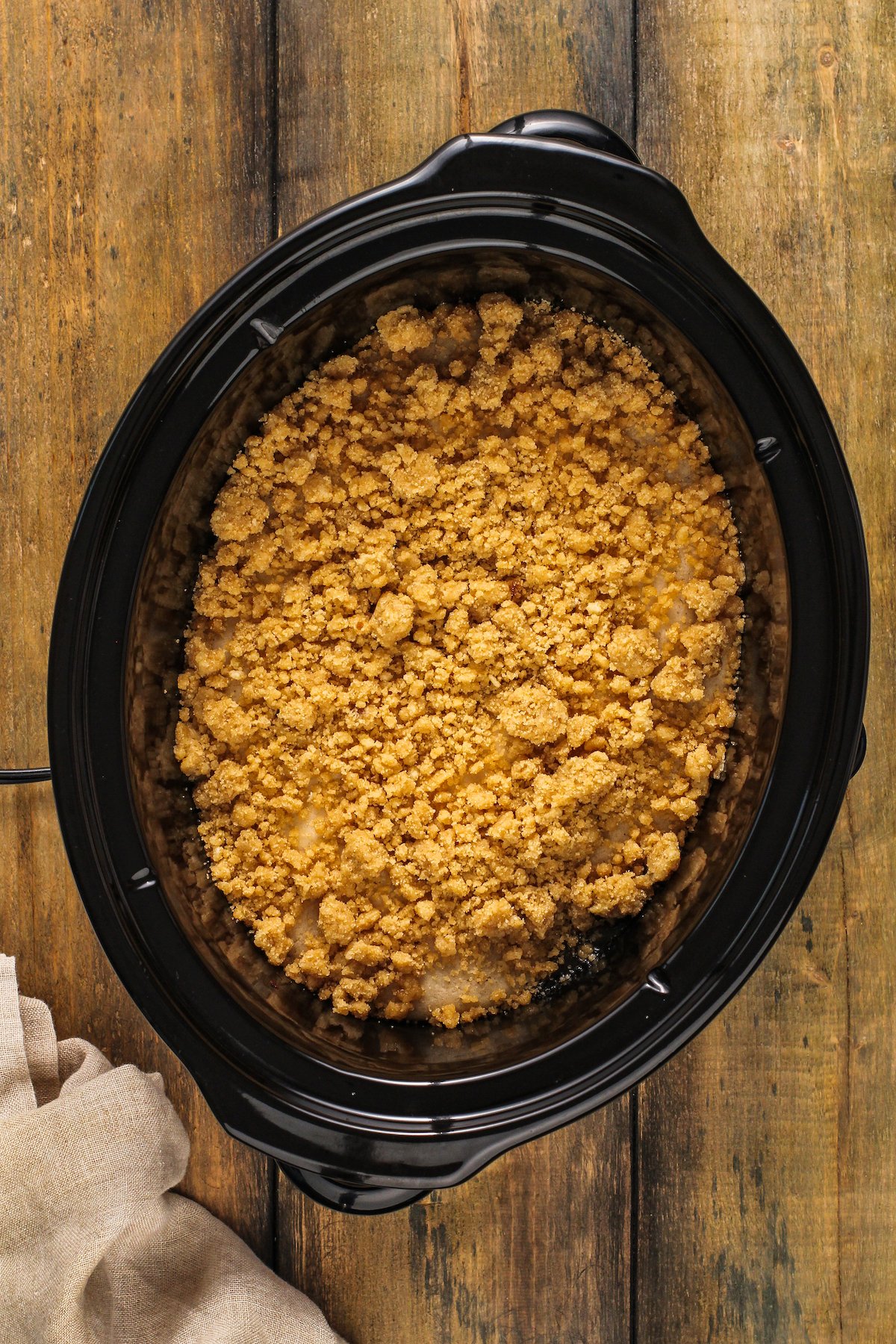 Brown sugar crumble is added overtop the partially cooked peach cobbler inside a crock pot.