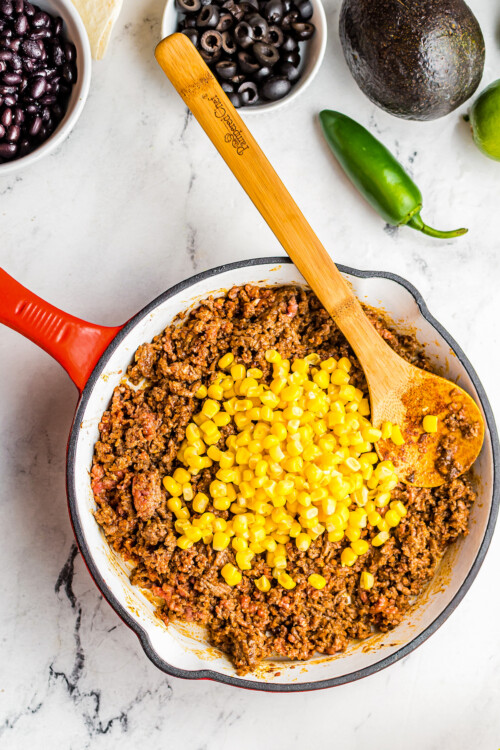 Corn and taco-seasoned beef in a skillet, with a wooden spoon resting in the skillet.