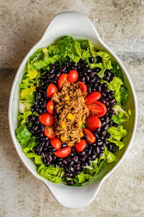An oval-shaped dish with lettuce, ground beef, black beans, and tomatoes arranged in rings.