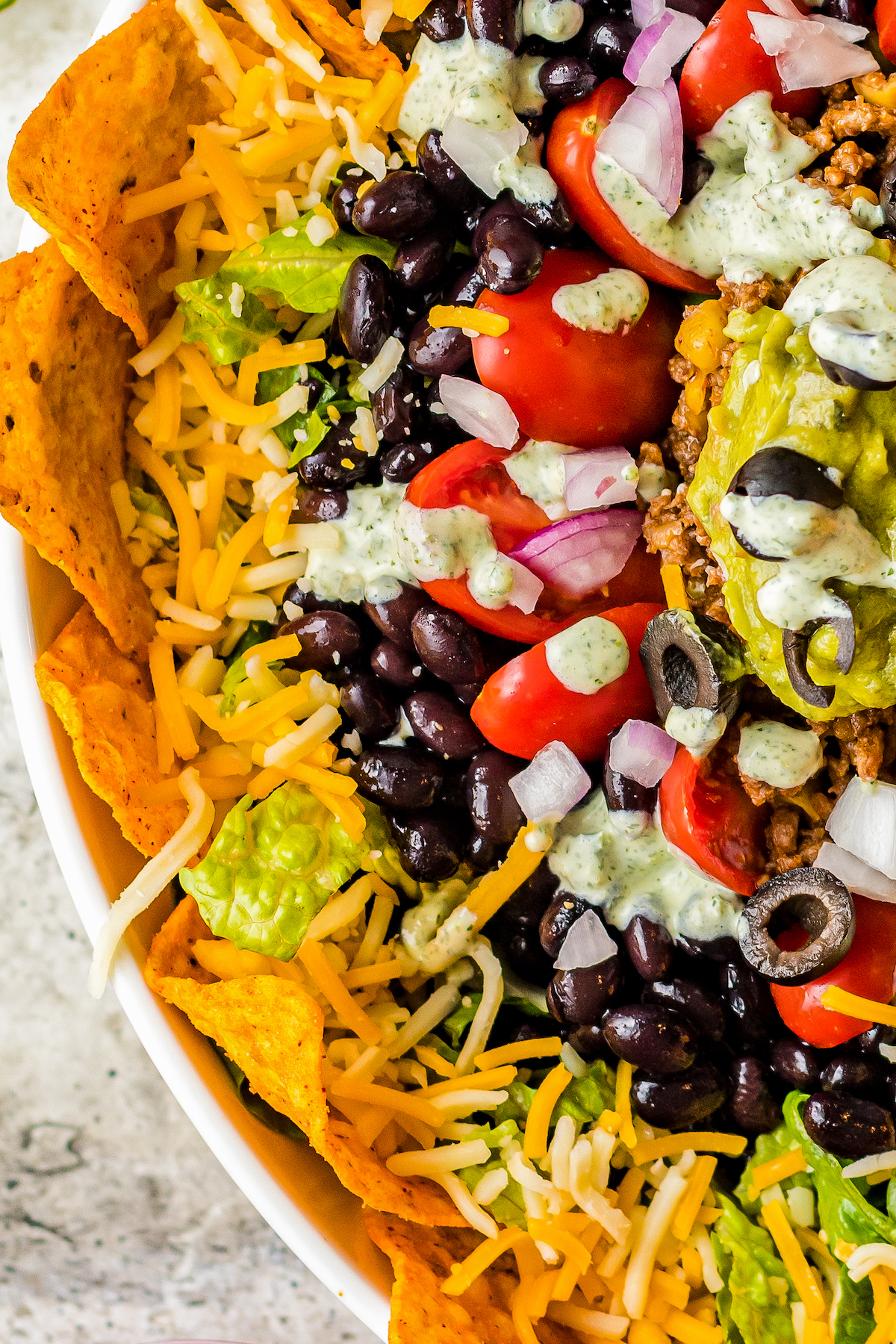 Close-up shot of an arranged salad, showing layers of Doritos, shredded cheese, balck beans, tomatoes, diced onions, and more.