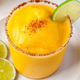 Frozen mango flavored margarita in a glass with a tajin rim and a lime garnish.