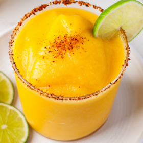 Frozen mango flavored margarita in a glass with a tajin rim and a lime garnish.