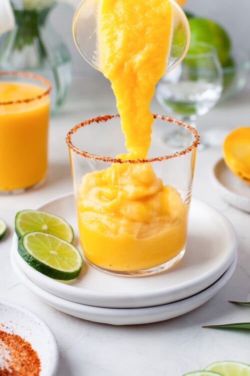 Frozen mango margarita being poured into a rimmed rocks glass.