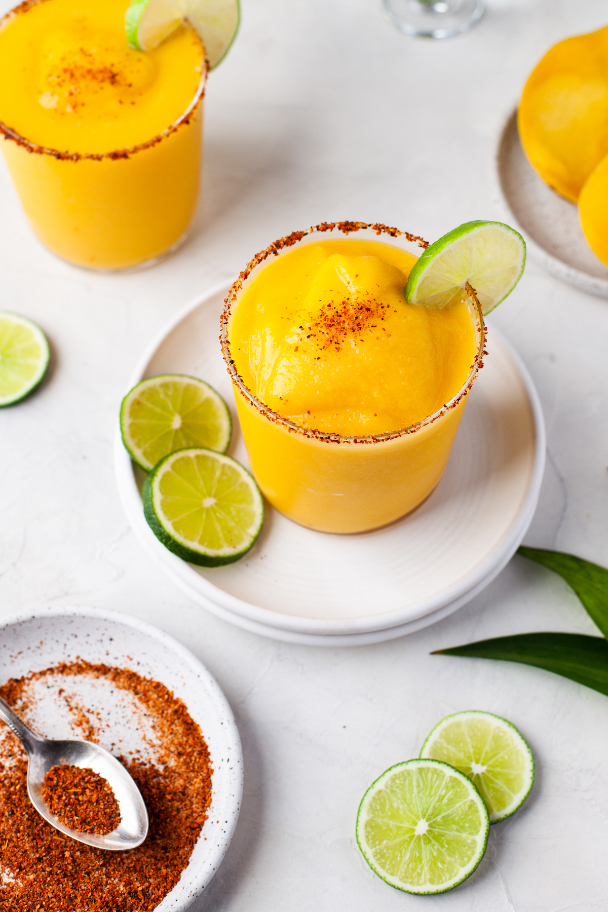 Two mango margaritas with lime for garnish, next to a plate of tajin.
