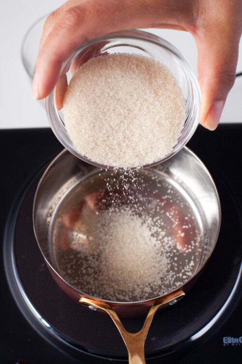 Sugar being poured into a small saucepan of water.