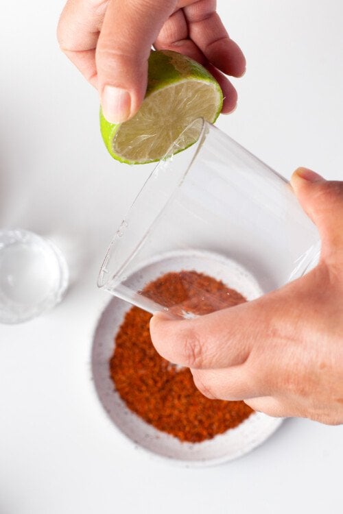 A glass being rimmed with lime, next to a small plate of tajin seasoning.