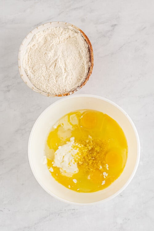 A bowl of dry ingredients next to a larger bowl of eggs, sour cream, milk, and other wet ingredients.