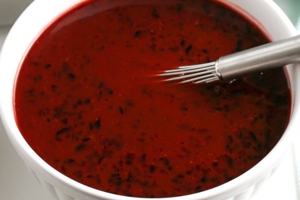 Easy 3-ingredient Grape Jelly Meatballs made in the crockpot or on the stovetop. Sweet, savory, and gone in minutes at every party! A white bowl filled with a mixture of bbq sauce and grape jelly with a metal whisk resting inside.