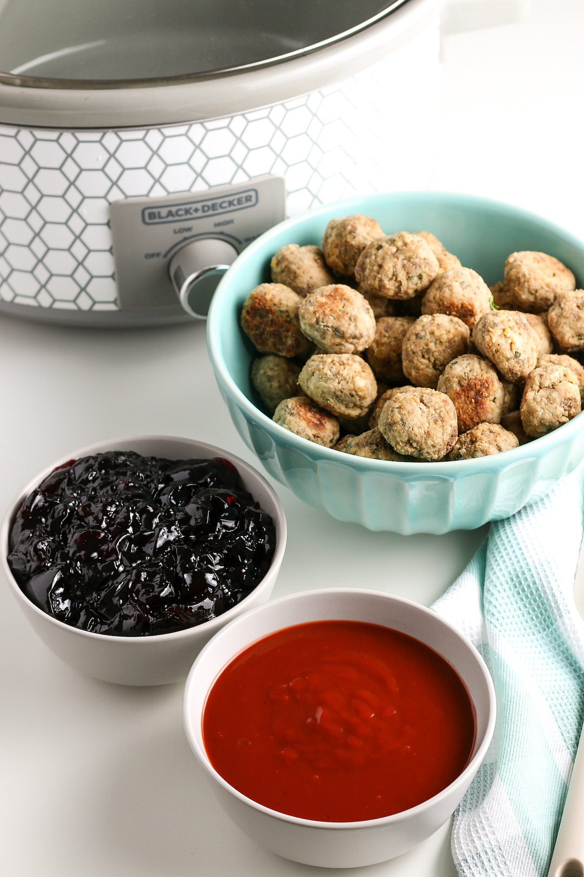 Cooked frozen meatballs, grape jelly, and barbecue sauce, next to a slow cooker.