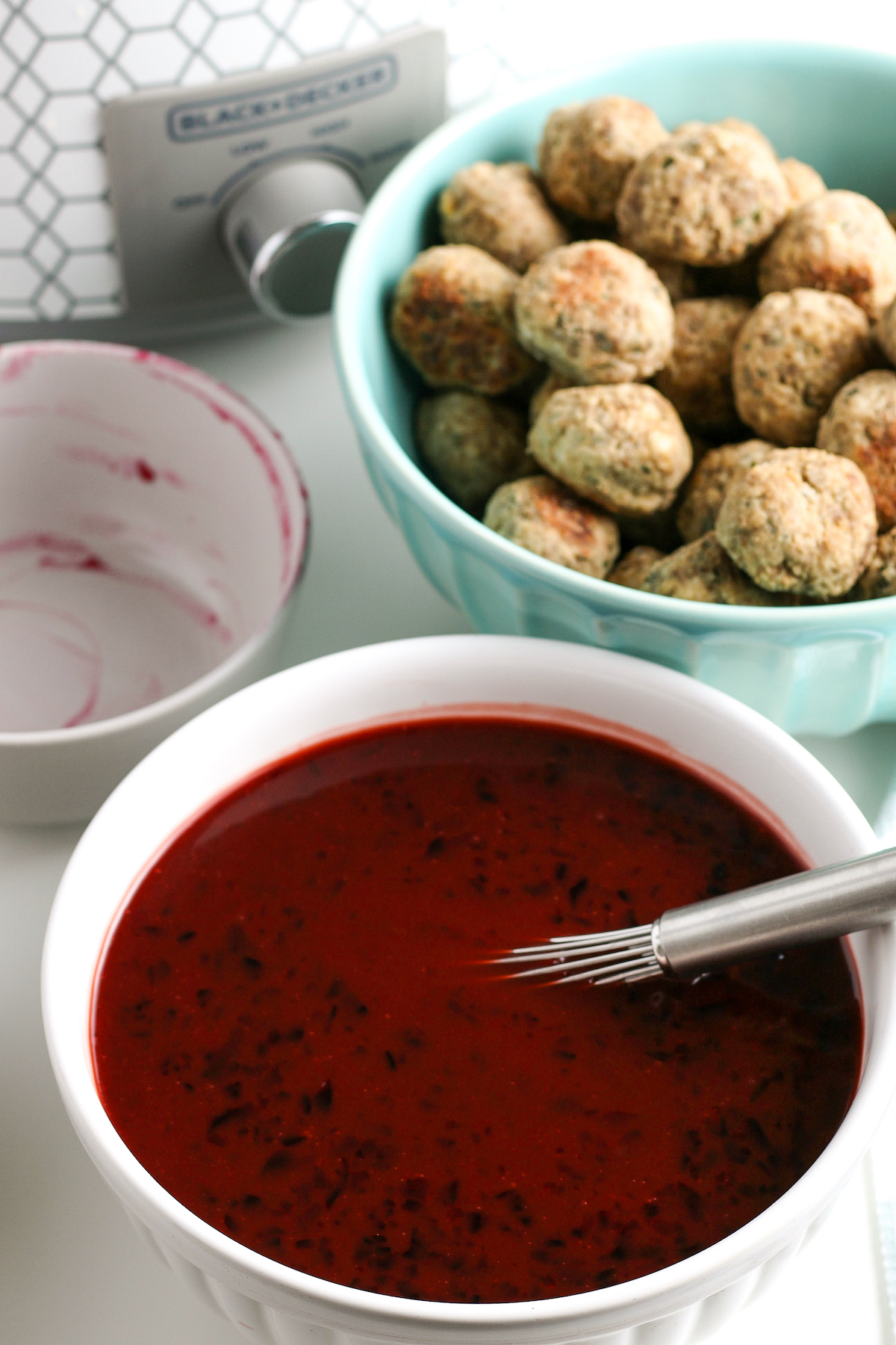 Whisked jelly and barbecue in a white mixing bowl. A dish of meatballs and a slow cooker are nearby on the work surface.