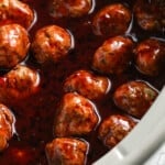 Close-up shot of grape jelly meatballs in a crockpot, to show the texture of the sticky sauce.