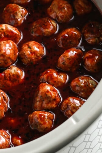 Close-up shot of grape jelly meatballs, to show the texture of the sticky sauce.