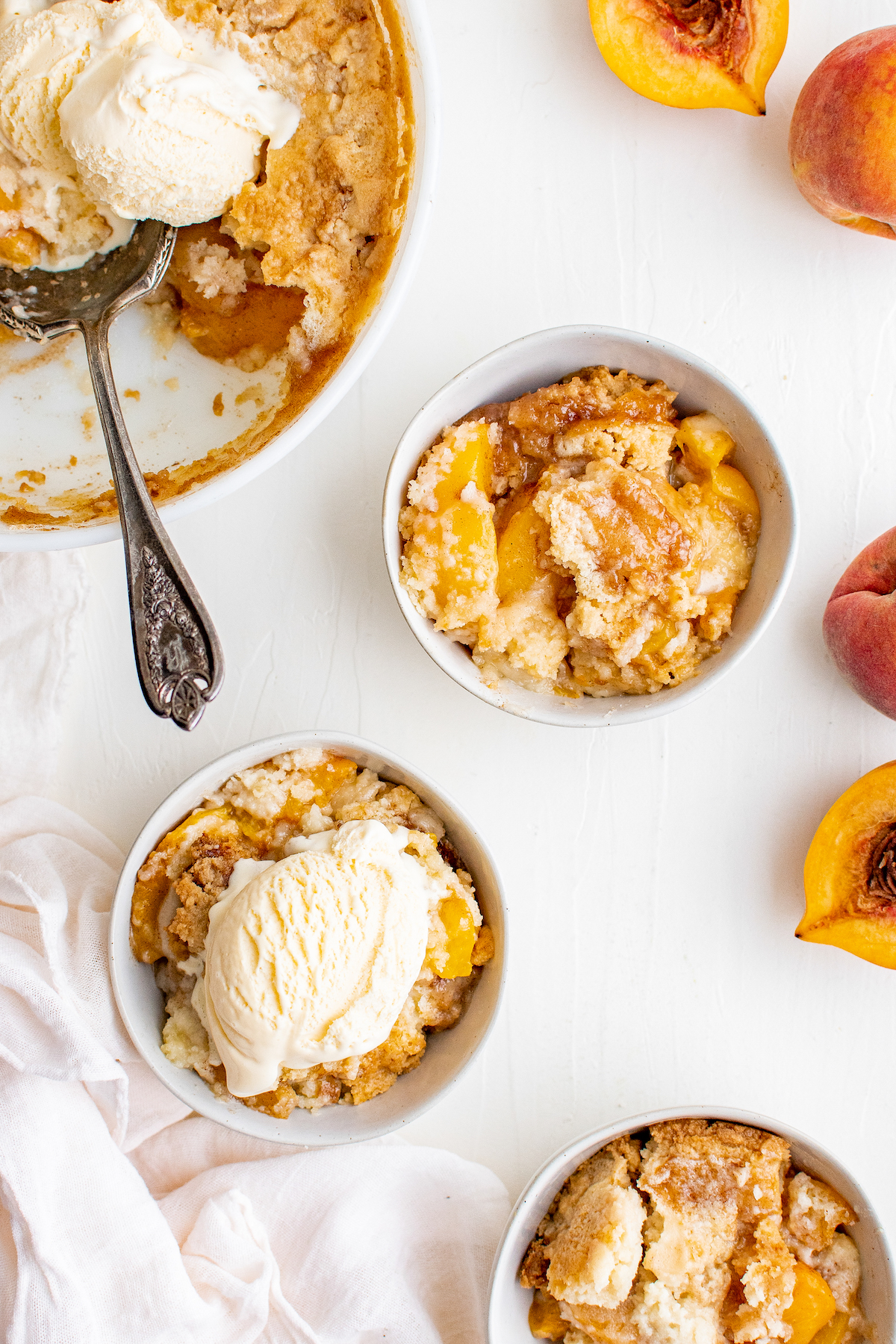 Overhead shot of a table with a peach dump cake, several small bowls served with the cake, and fresh peaches.